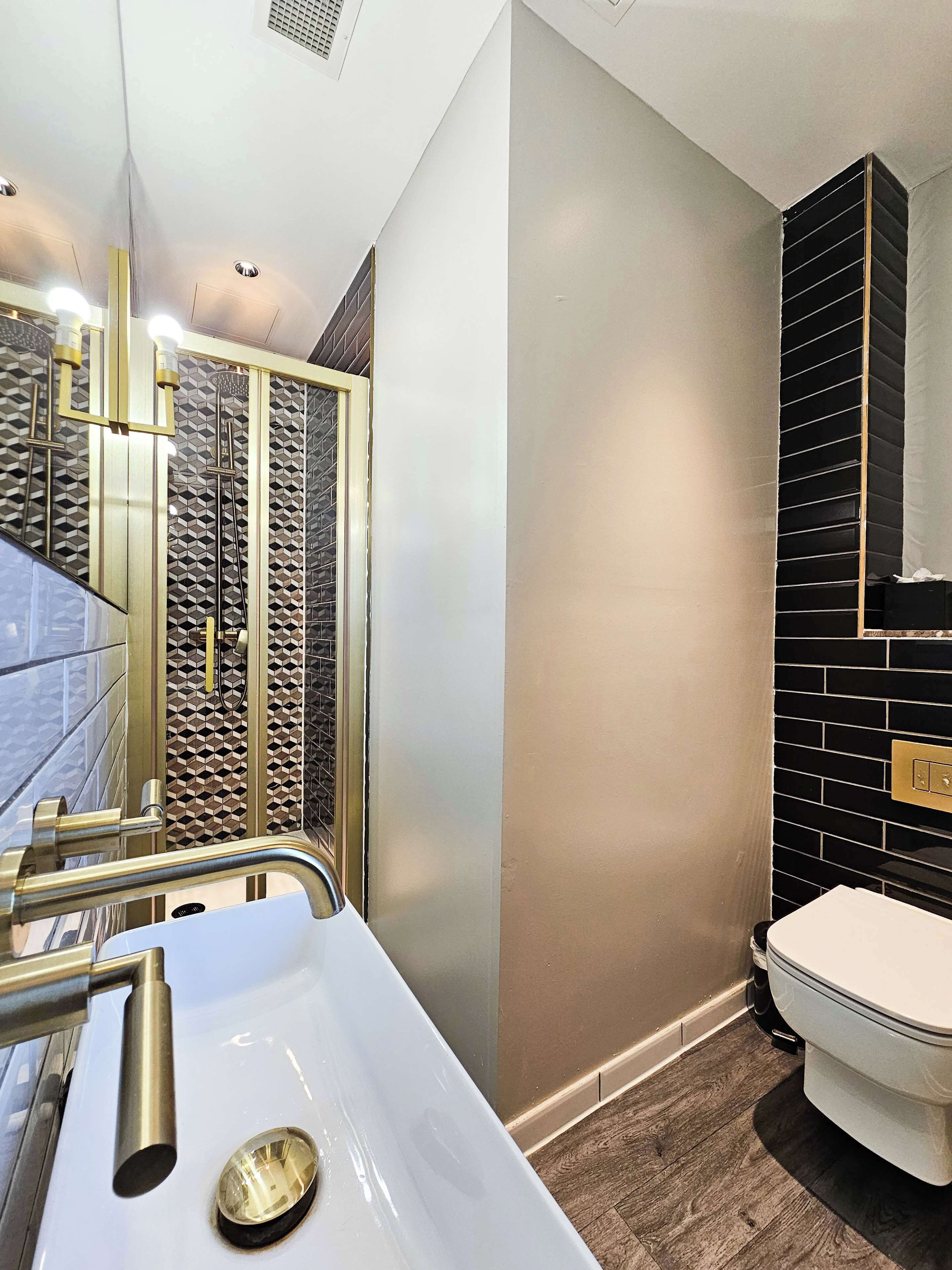 Ein modernes Badezimmer mit einem weißen Waschbecken, goldenen Armaturen und einer Wand mit schwarzen Fliesen.