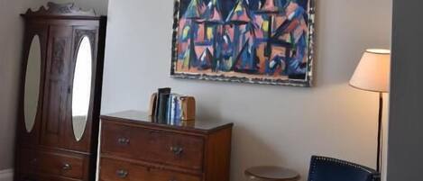 Una habitación con un aparador de madera, un sillón azul, un cuadro en la pared y una araña.