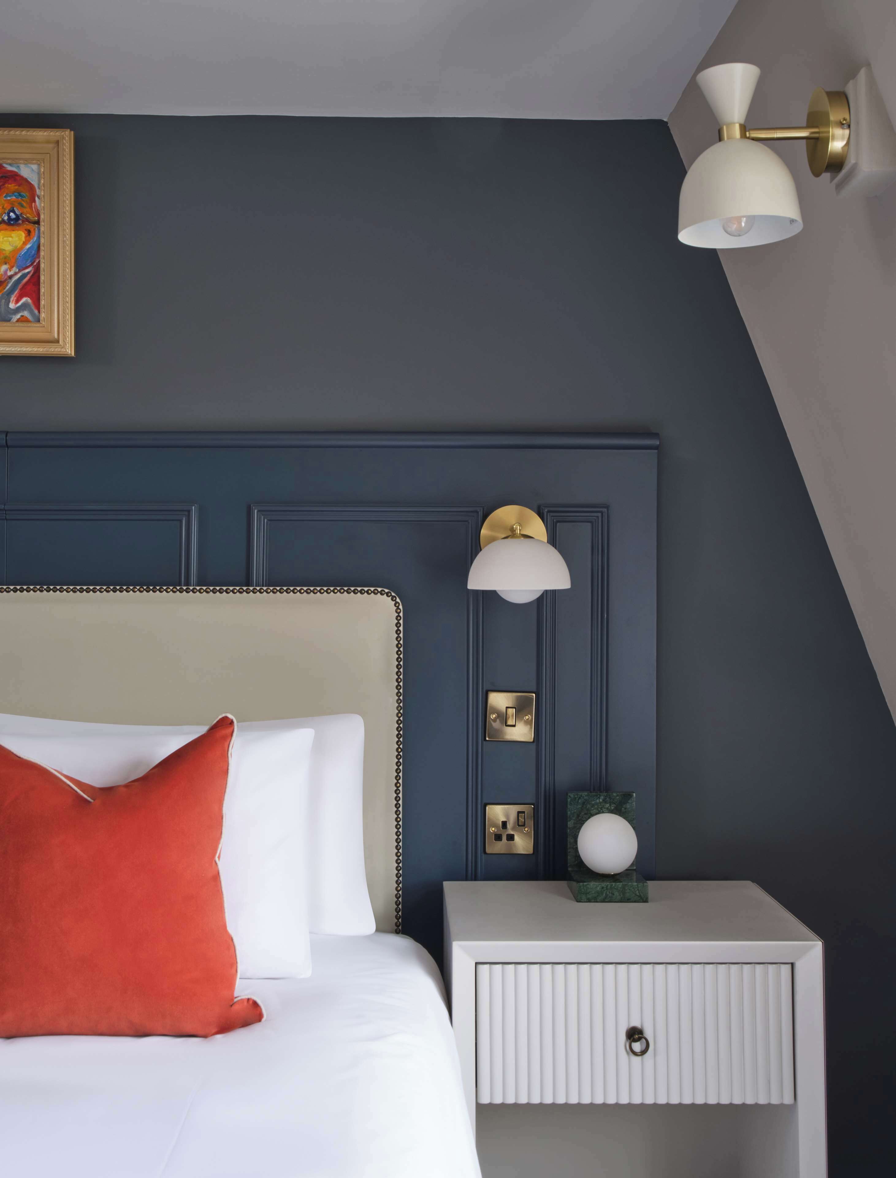 Un dormitorio con una cama, una mesita de noche, una lámpara de pared y un cuadro.