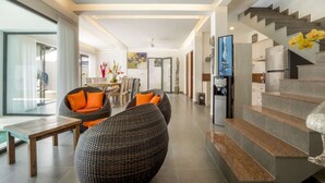 A modern living room with wicker furniture, a dining area, and a staircase leading to a kitchen. - Rent a Luxury Villa in Bali Close to the Beach, Bali Villa 2057 (Bali)