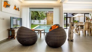 A modern living room with a pool view, wicker furniture, and a dining area with a table and chairs. - Rent a Luxury Villa in Bali Close to the Beach, Bali Villa 2057 (Bali)
