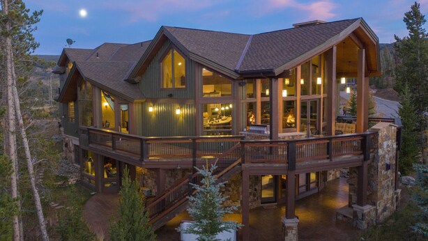 Ein großes, mehrgeschossiges Holzhaus mit einer Terrasse und Außenbereich zum Sitzen, umgeben von Bäumen.