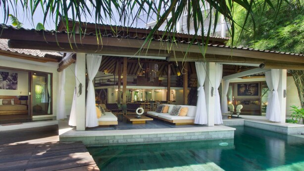 A poolside area with a wooden deck, a lounge with sofas and a dining table, and a large indoor space with a high ceiling and wooden beams. - 5 Star Villa in Bali, Minutes from the Beach, Bali Villa 2065 (Bali)
