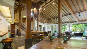 A spacious indoor area with a high ceiling, wooden beams, and a large dining table with chairs. There are decorative items on the table, and a staircase is visible in the background. - 5 Star Villa in Bali, Minutes from the Beach, Bali Villa 2065 (Bali)
