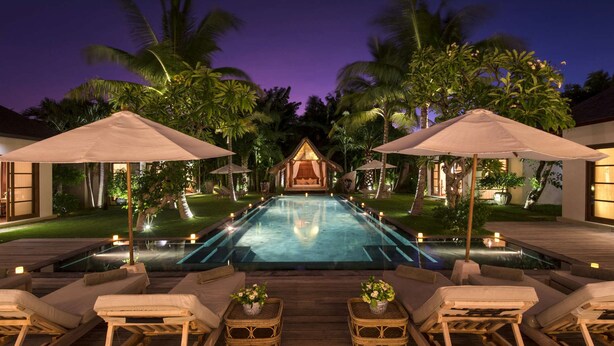 Un espace aménagé au bord de la piscine, avec des chaises longues, des parasols et un petit bâtiment doté d’un auvent.