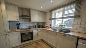 Una cocina moderna con armarios blancos, horno empotrado, pileta y una ventana con persianas.