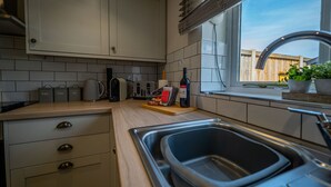 Una cocina moderna con armarios blancos, un lavamanos de acero inoxidable y una ventana con vista a una cerca de madera.