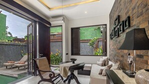 A modern living room with a sofa, a dining table, and a chair. There is a large window with a view of greenery outside. - Exclusive Holiday Villa with Private Pool and Staff in Umalas, Bali Villa 2079 (Bali)