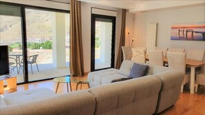 A modern living room with a large sofa, a glass coffee table, and a dining area with wicker chairs. - Villa André con Piscina, Barbacoa, Wifi & Satélite (Vícar)