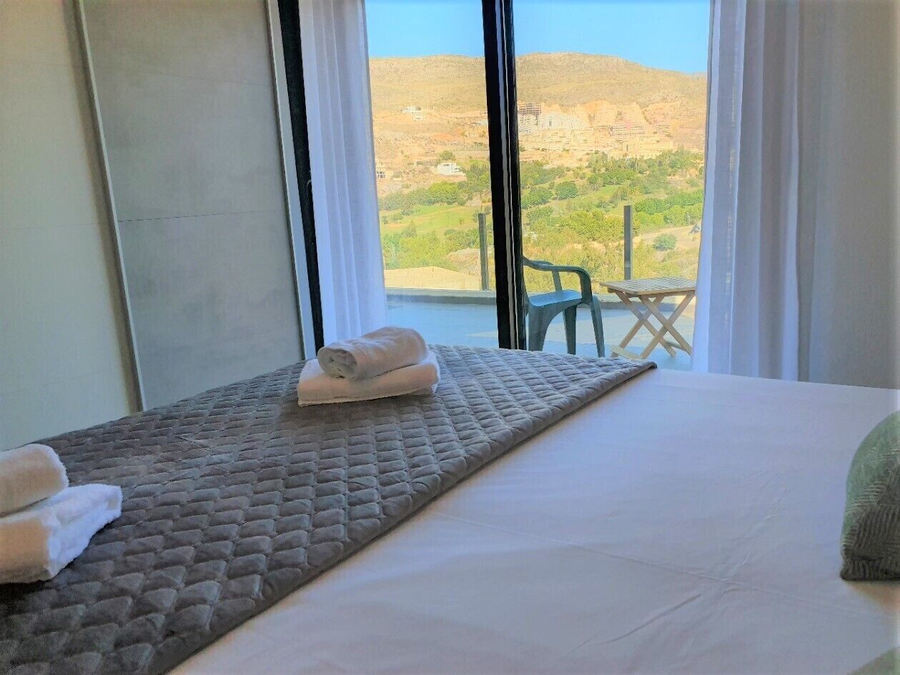 A hotel room with a bed, a view of a mountainous landscape, and a chair outside the window.