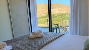 A hotel room with a bed, a view of a mountainous landscape, and a chair outside the window. - Villa André con Piscina, Barbacoa, Wifi & Satélite (Vícar)