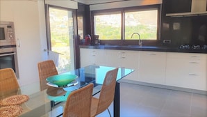 A modern kitchen with a glass dining table, wicker chairs, and a view of greenery outside. - Villa André con Piscina, Barbacoa, Wifi & Satélite (Vícar)