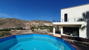 A modern building with a swimming pool, offering a view of a hillside town. - Villa André con Piscina, Barbacoa, Wifi & Satélite (Vícar)