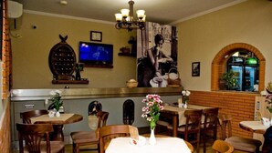 A restaurant interior with wooden tables and chairs, a television mounted on the wall, and a brick archway. - 4 Stinet Hotel (Vlorë)