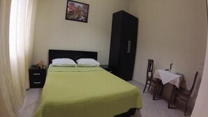 A bedroom with a bed, a nightstand, a wardrobe, a small table with a chair, and a painting on the wall. - 4 Stinet Hotel (Vlorë)
