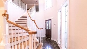 Un escalier avec des rampes blanches et des mains courantes en bois menant à une porte sombre ornée d’un vitrail.