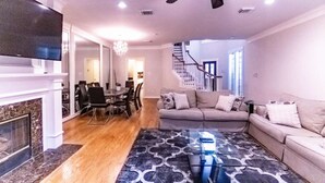 Un salon avec une cheminée, un coin repas, un escalier et un téléviseur.