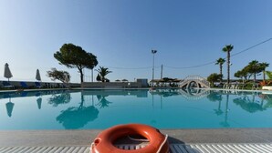 Una piscina con un flotador salvavidas en el borde, rodeada de palmeras y un paseo cubierto.