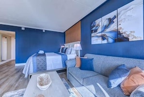 A room with a bed, a sofa, a coffee table, and a painting on the wall.