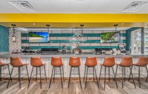 A bar area with a counter, multiple screens, and bar stools.