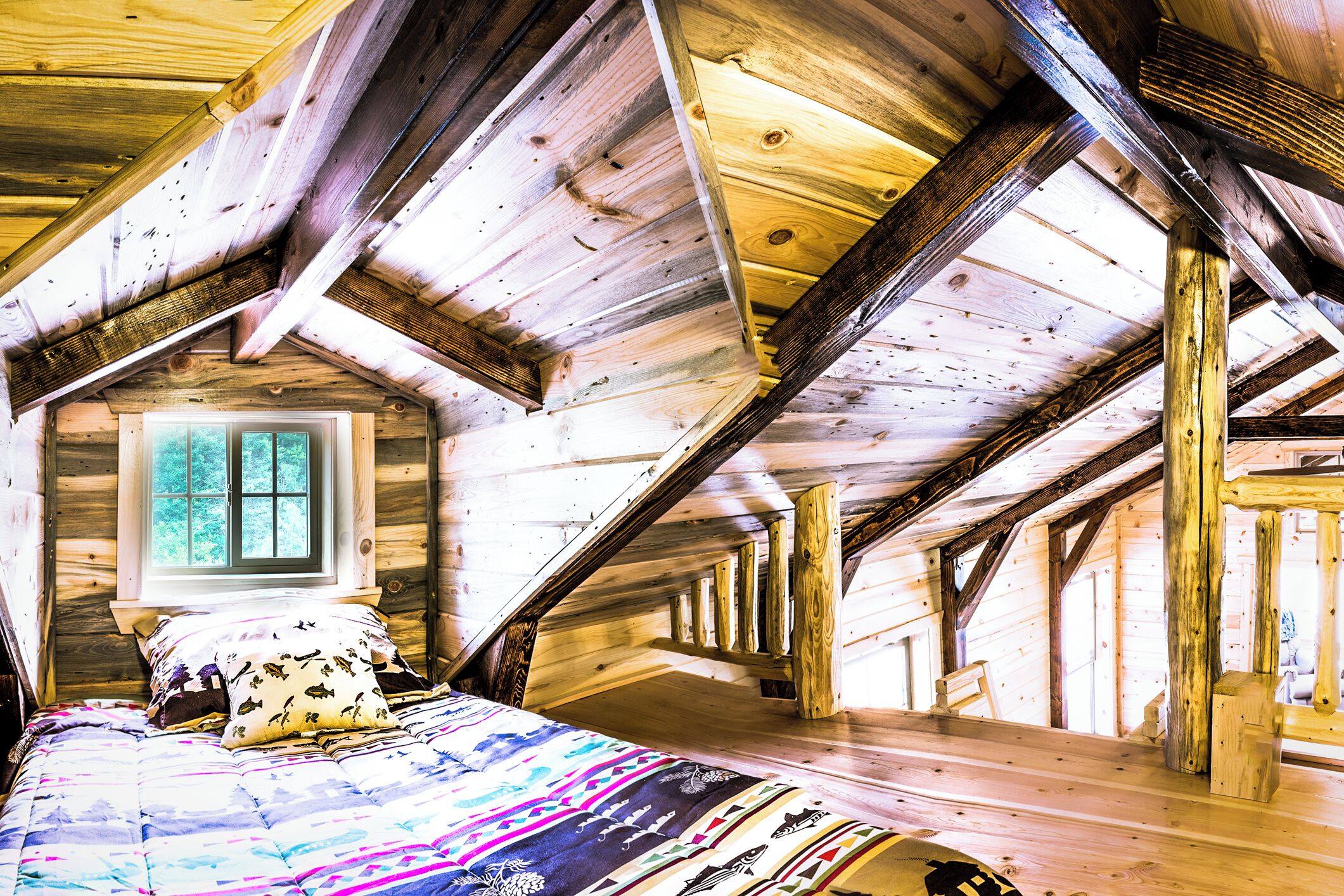Un dormitorio estilo ático con techo inclinado, una ventana y una cama con colcha colorida.