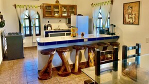 A kitchen with a central island, wooden stools, a refrigerator, and a microwave. - Casa El Delfin, 1st Floor - Main Level- Estacahuite (Estacahuite)