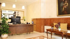 A reception area with a desk, computer, and a painting on the wall. - Basilica Hotel (Rome)