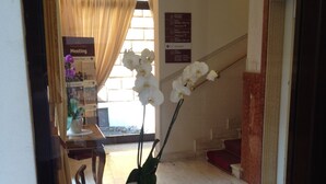 A hotel reception area with a reception desk, a potted orchid, and directional signs. - Basilica Hotel (Rome)