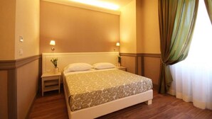 A hotel room with a large bed, two bedside lamps, a nightstand with a vase of flowers, and a window with curtains. - Basilica Hotel (Rome)