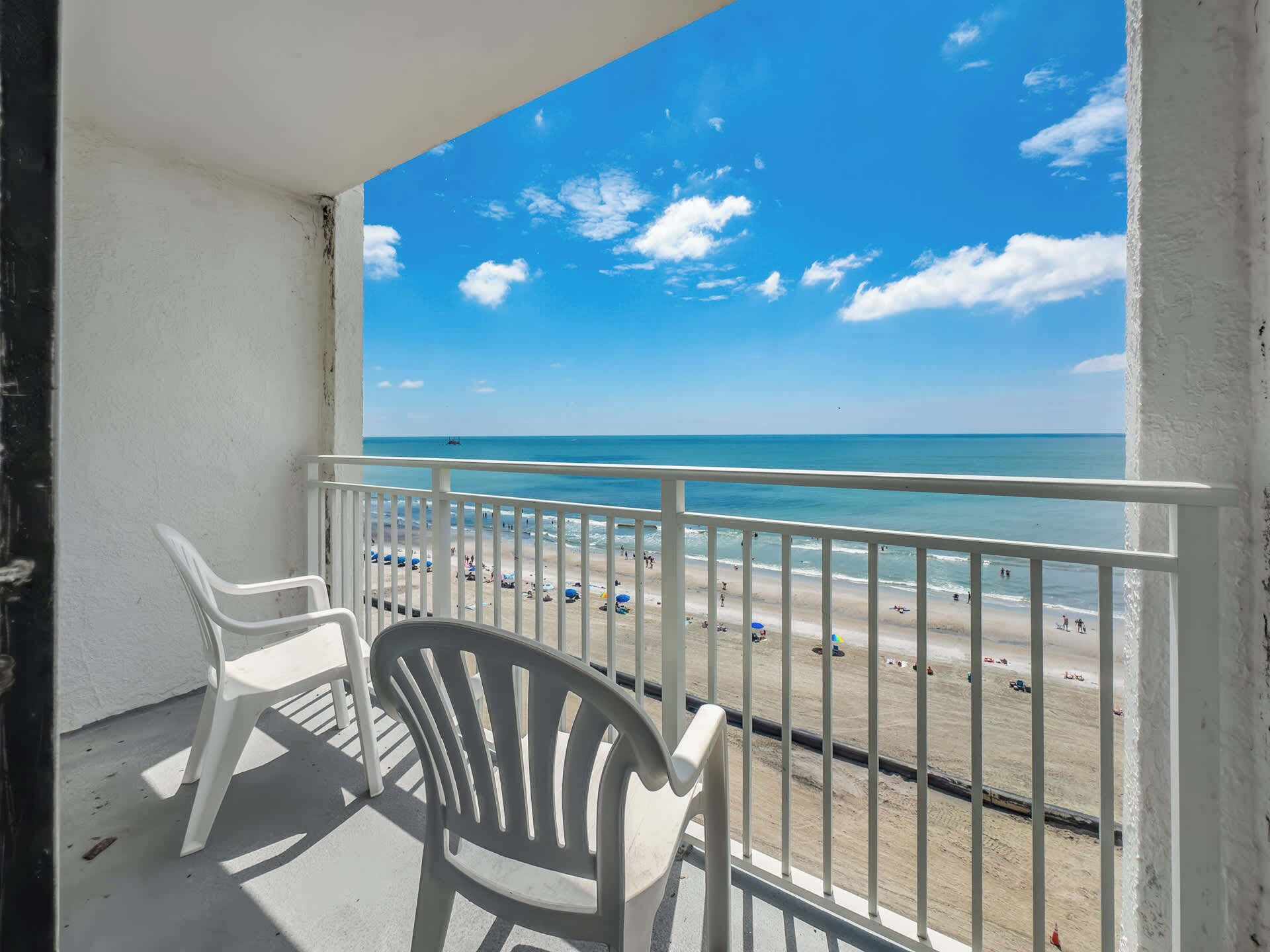 A balcony with white chairs, a view of a beach, and a clear blue sky.