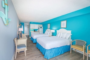 A hotel room with two beds, a desk, a chair, and a kitchenette.