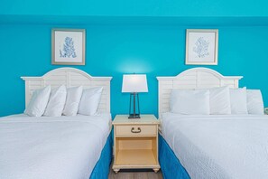 A room with two beds, a nightstand with a lamp, and two framed wall art pieces.