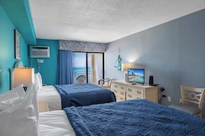 A hotel room with two beds, a desk with a computer, a TV, and a view of the ocean.