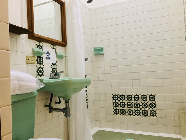 A bathroom with a green sink, a mirror, a shower curtain, and patterned tiles. - Hotel Mansión Virreyes (San Miguel de Allende)