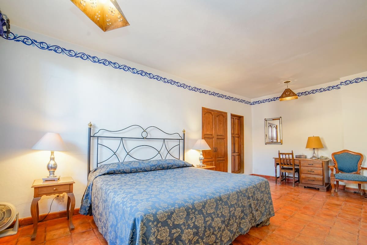 Ein Schlafzimmer mit einem Bett, zwei Nachttischen, einem Schreibtisch, einem Sessel und einem Kleiderschrank.
