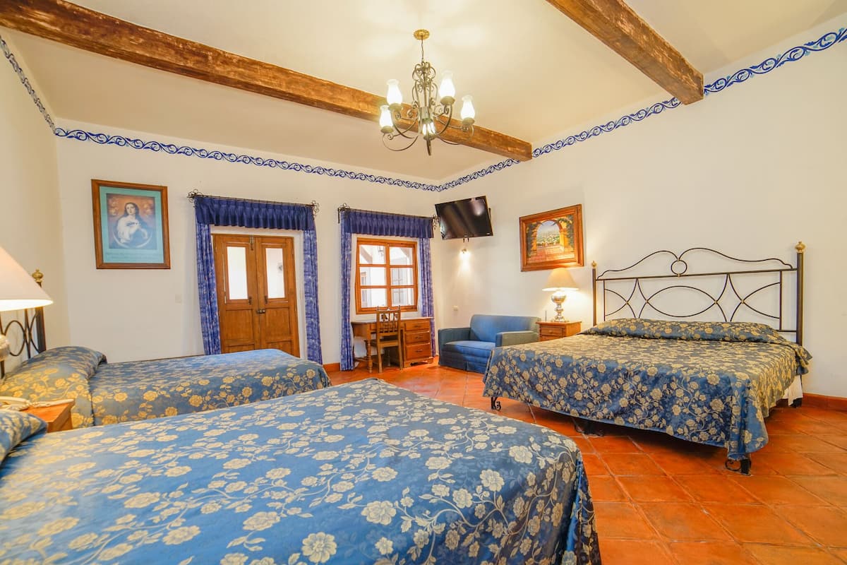 Ein Schlafzimmer mit zwei Betten, einem Schreibtisch, einem Stuhl, einem Fernseher und einer Kandelaber.