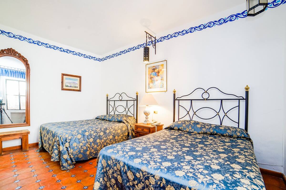 Ein Zimmer mit zwei Betten, Holzboden, einem Spiegel und einer Lampe.