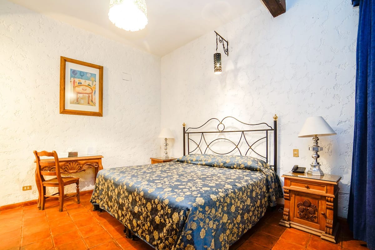 Ein Schlafzimmer mit Bett, Schreibtisch, Stuhl, Nachttisch und einer Wandlampe.