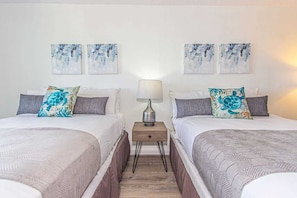 A hotel room with two beds, each with a patterned bedspread, a nightstand with a lamp, and two wall-mounted paintings.