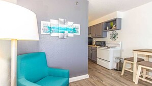A living room with a teal sofa, a dining area with a wooden table and chairs, a kitchen with a stove and cabinets, and a gray wall with artwork. - Sea Mist 51610 (Myrtle Beach)