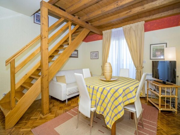 A room with a wooden staircase, a white sofa, a table with a plaid tablecloth, a television, and a vase. - VILLA ROSSELLA 1 Two-Bedroom Apartment (Prunella) (Rovinj)