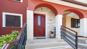 A red door with a stone wall, a staircase with a metal railing, and a small potted plant on the steps. - VILLA ROSSELLA 1 Two-Bedroom Apartment (Prunella) (Rovinj)