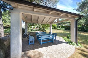 A covered outdoor seating area with stone flooring, a barbecue grill, and blue benches. - VILLA ROSSELLA 1 Two-Bedroom Apartment (Prunella) (Rovinj)
