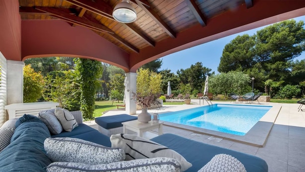 A covered outdoor seating area with a pool, lounge chairs, and a view of the surrounding garden. - VILLA ROSSELLA 1 Two-Bedroom Apartment (Prunella) (Rovinj)