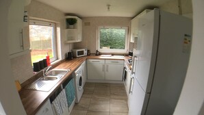 A compact kitchen with a washing machine, a microwave, and a refrigerator. - Phoenix House (Corby)