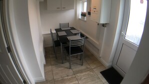A compact kitchen with a dining table, chairs, a white cabinet, and a refrigerator. - Phoenix House (Corby)