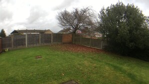 A grassy backyard with a wooden fence, a tree, and a house in the background. - Phoenix House (Corby)