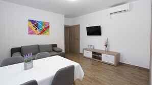 Un salon moderne avec un canapé blanc, une table à manger et un téléviseur fixé au mur.