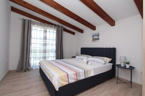 Un dormitorio con cama, mesita de noche, una pequeña mesa y una ventana con cortinas.
