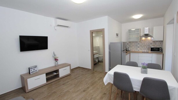 Un appartement moderne comprenant un coin repas, une cuisine et un téléviseur fixé au mur.